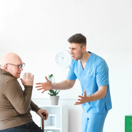 Frustrated healthcare worker in blue scrubs arguing with elderly man using a cane in a medical office setting.