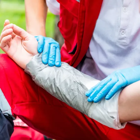 Paramedic wearing gloves applying a bandage to an injured person's arm outdoors during emergency care.