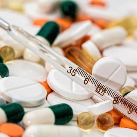 Glass thermometer resting on assorted white, orange, green capsules, and round tablets in various sizes and colors