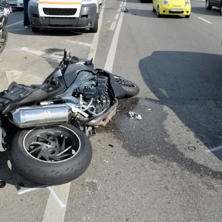 Black motorcycle lying on its side after an accident on a city street with nearby parked and moving cars.