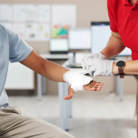 Medical professional in red shirt bandaging a man's injured hand in a clinic setting