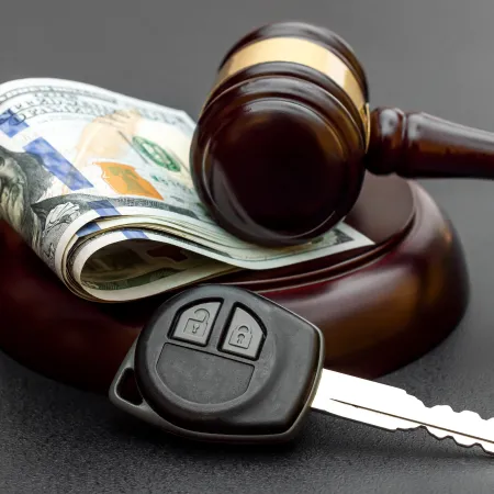 Judge's gavel resting on money and a car key on a dark surface symbolizing auto auction or legal car sale.