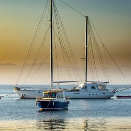 Two sailboats anchored on calm water during a golden sunset with distant mountains in the background