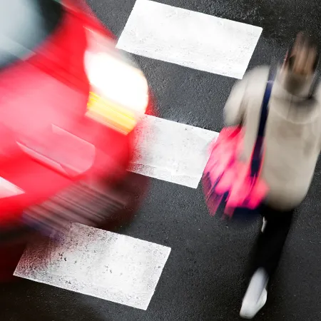 Blurred image of a red car speeding past a pedestrian crossing with a person carrying a pink bag.