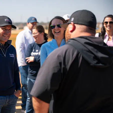Group of casually dressed people smiling and chatting outdoors on a sunny day in an open area.
