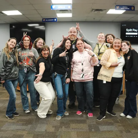 Group of diverse coworkers posing cheerfully in a modern office with computers and desks in the background.