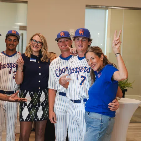 Group of smiling people including baseball players in Chargers uniforms and staff inside a bright indoor space.