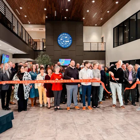 Large group cutting a red ribbon at the Tabernacle Baptist Church building interior grand opening ceremony.