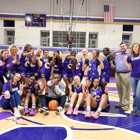 High school girls basketball team and coaches posing with smiles and peace signs on gym court