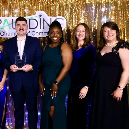 Group of six people dressed formally posing with award in front of gold sequin backdrop at Paulding Chamber event