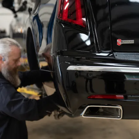 Mechanic with grey beard working on the rear wheel of a black car in a garage workshop.
