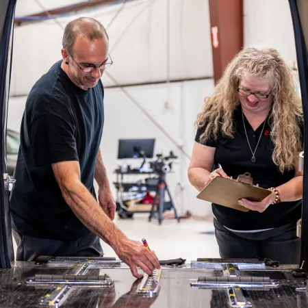 Two people inspecting and marking a large metal sheet on a worktable inside a workshop.