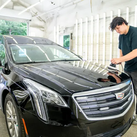 Technician polishing the hood of a black Cadillac limousine in a well-lit garage.
