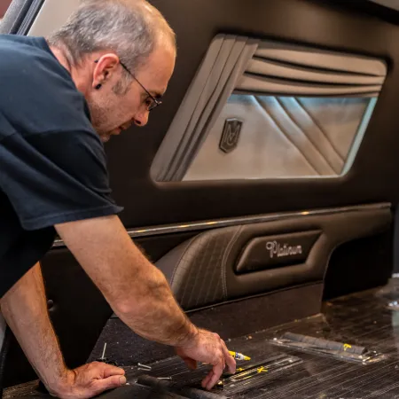 Man inspecting interior car panel labeled Platinum, working on black and gray upholstery with window and lighting.