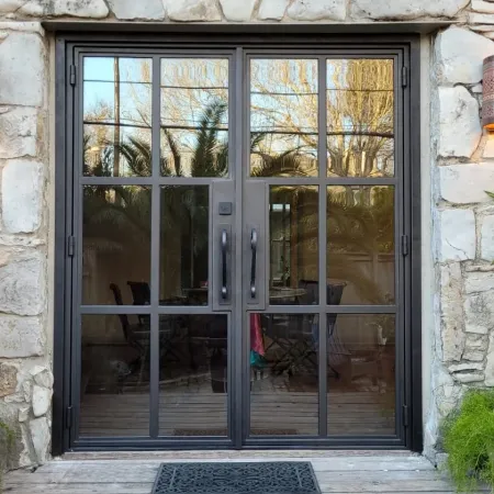 Black metal-framed glass double doors set in stone wall with outdoor plants and decorative wall sconces.