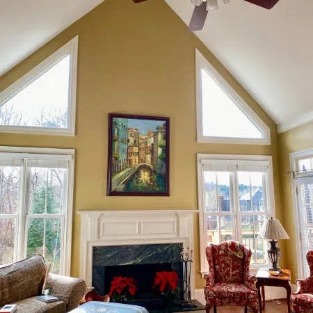Cozy living room with vaulted ceiling, large windows, fireplace with poinsettias, and red floral armchairs.