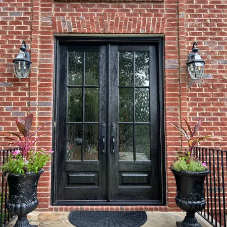 Elegant black double doors framed by brick and stylish planters with vibrant flowers.