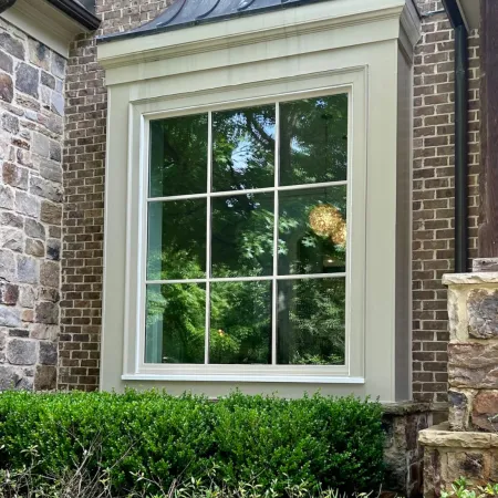 Beautiful home exterior featuring a large beige picture window framed by green foliage and stone accents.