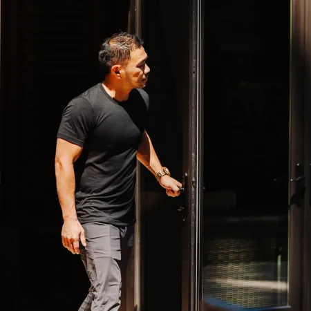 Man in black t-shirt and gray pants opening a glass door into a dark room