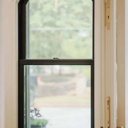 Arched black-framed window with white trim overlooking a blurred outdoor scene, next to a green chair and door handle.