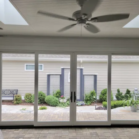Sliding glass patio doors open to a landscaped patio with benches, plants, and a ceiling fan inside.