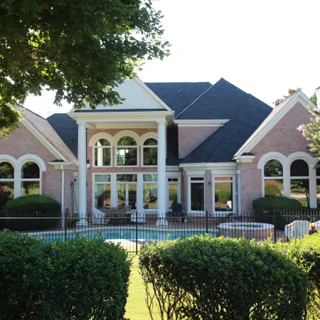 Large suburban house with brick facade, arched windows, black roof, fenced backyard and swimming pool