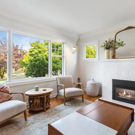 a living room with a fireplace and large windows with white frames overlooking trees