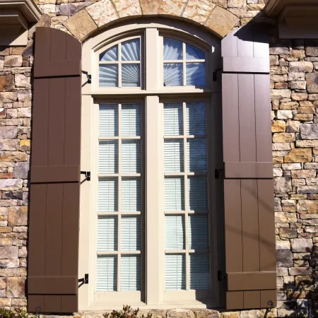 a window in a stone building with custom archtop shutters