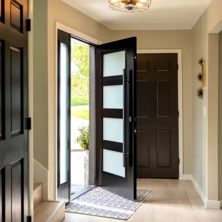Modern home entryway with black front door open, glass panels, light wood flooring, and beige walls.