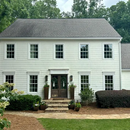 Charming two-story white house with dark front door, green landscaping, and stone pathway.