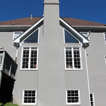 Rear view of a two-story gray house with multiple white-framed windows and a raised wooden deck under a clear blue sky