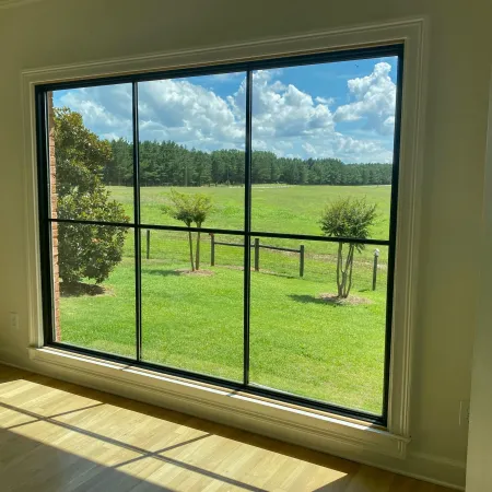 A large picture window with grill lines for aesthetic detail overlooks field