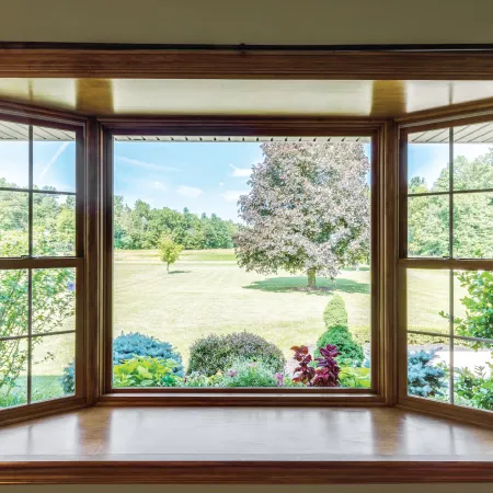 Bay window with wood trim overlooks a manicured front yard