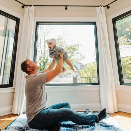 A man playing with a baby in front of casement and picture windows from Infinity from Marvin fiberglass replacement windows. 