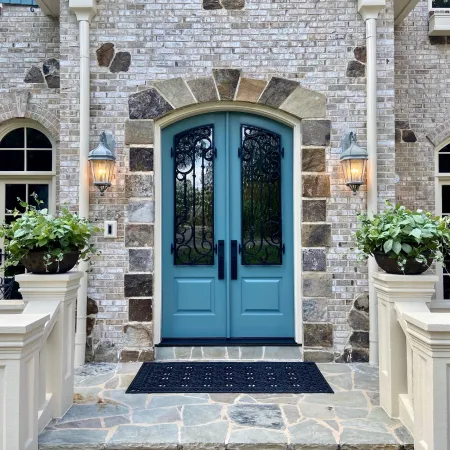Blue arched double front entry doors with privacy glass, iron grates, and black hardware on stone house