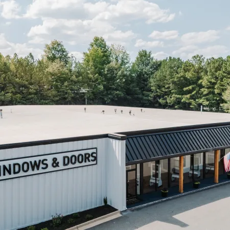Modern commercial building with Infinity Windows & Doors signage surrounded by trees under a cloudy sky.