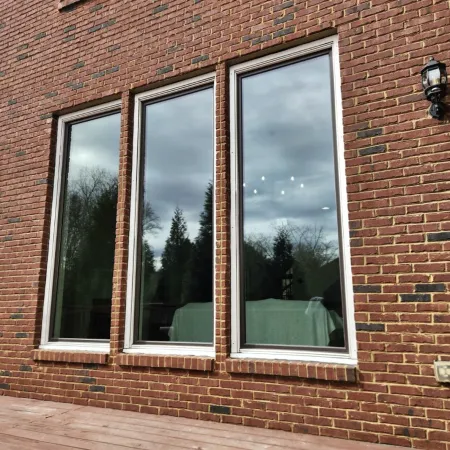 Three large reflective windows on a brick house wall overlooking a wooden deck with outdoor light fixture