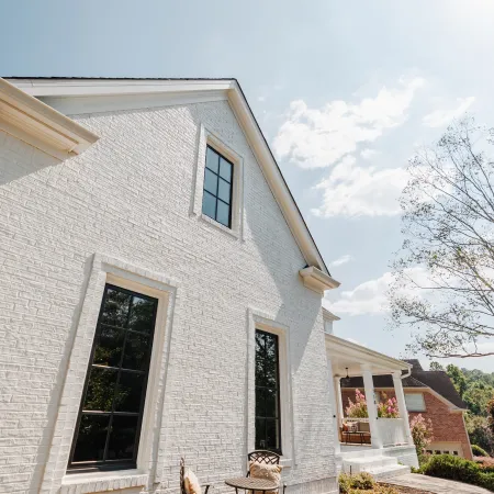 White brick house exterior with black windows, small patio table and chairs, and clear sunny sky.