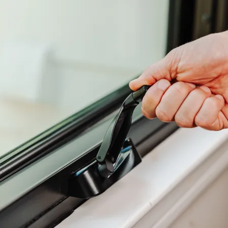 Hand gripping and opening a black window handle on a modern glass window.