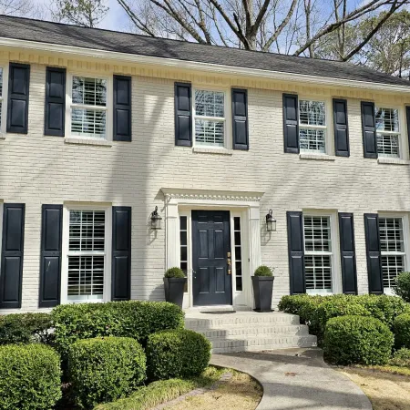 Elegant two-story white brick house with black shutters and manicured landscaping.
