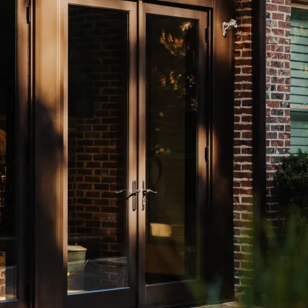 Brown framed glass double doors with metal handles on brick house exterior under sunlight.