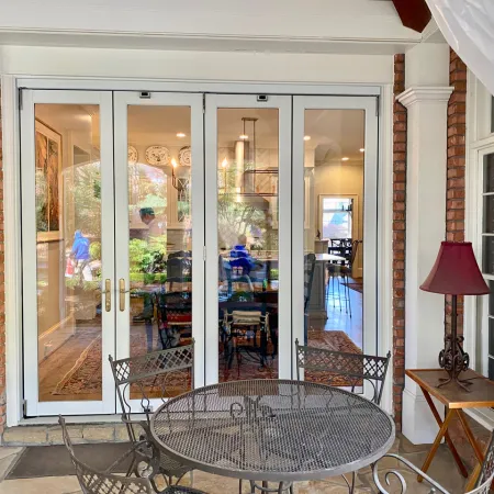 Outdoor patio with metal table and chairs in front of glass sliding doors leading to a dining room inside a brick house.
