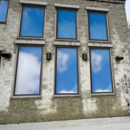 Stone building facade with six rectangular windows reflecting blue sky and clouds, with decorative wall sconces.