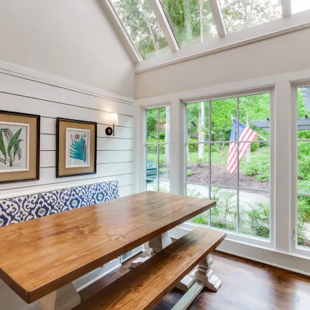 bright dining room with wooden table and large fiberglass windows with a bright view to exterior yard