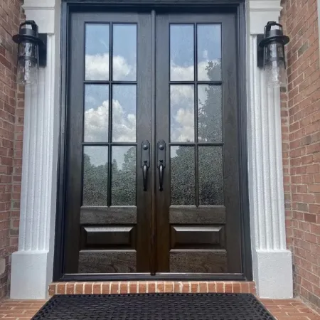 Double dark wood front doors with glass panels and black handles, flanked by white columns and black outdoor lanterns.