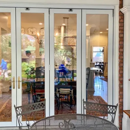 Outdoor wrought iron table and chairs on patio with white framed glass doors showing indoor dining area.