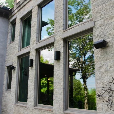 Stone house exterior with large reflective windows showing trees and sky on a clear day.
