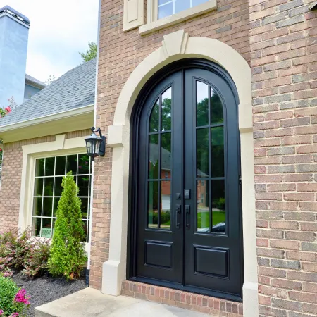 Brick house with black arched double entry doors made with iron and glass.