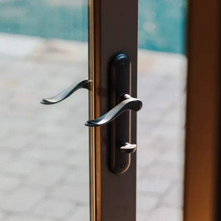 Close-up of black metal door handle on glass door with a blurred outdoor stone patio background.