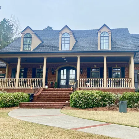Large brick house with a tall front porch, multiple windows, arched doorway, red brick steps, and front lawn.